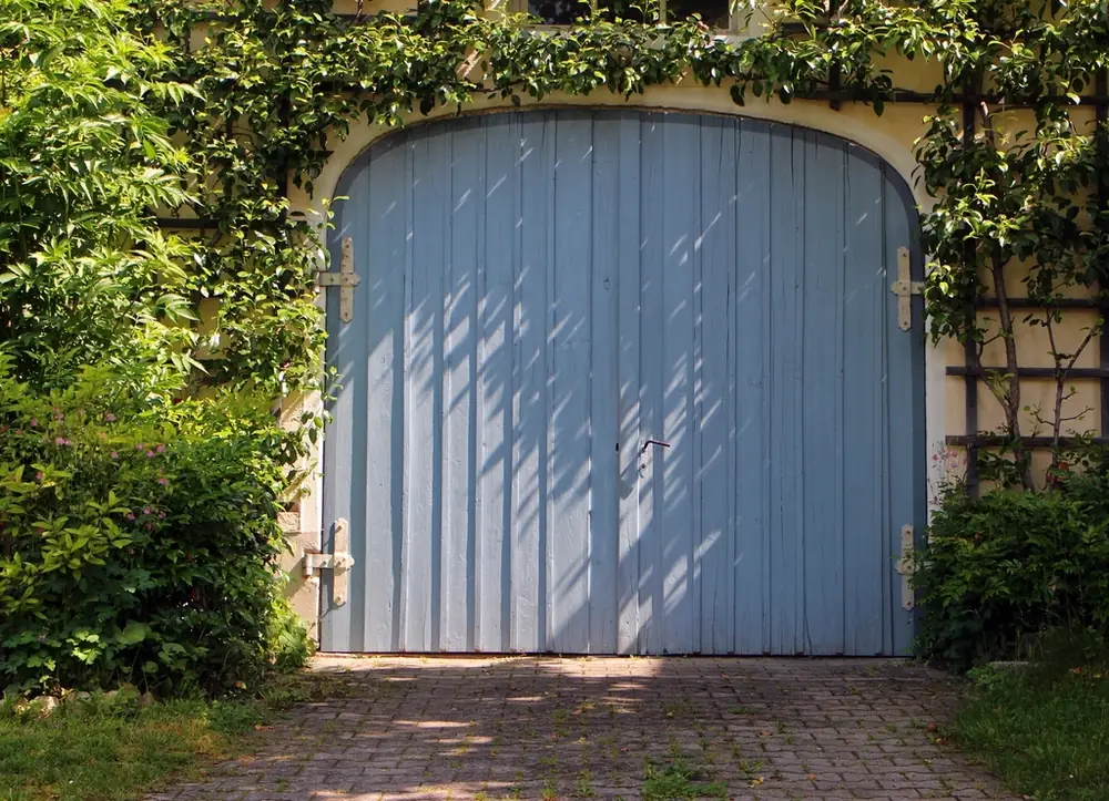 Arched blue-painted wooden garage door framed by climbing vines