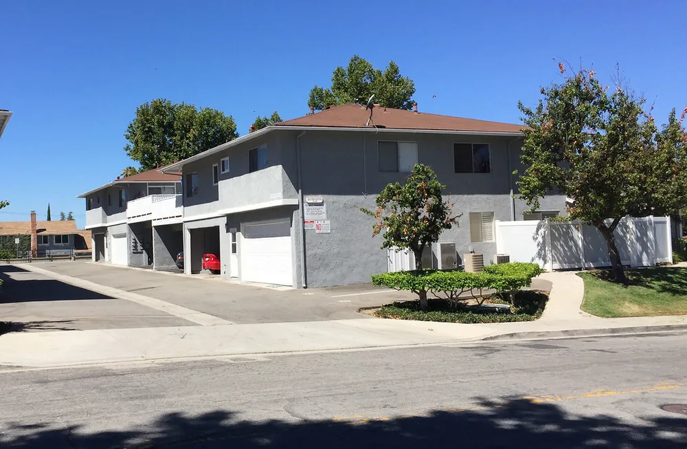 Two-story townhomes with a row of white attached garage doors along a sunny street