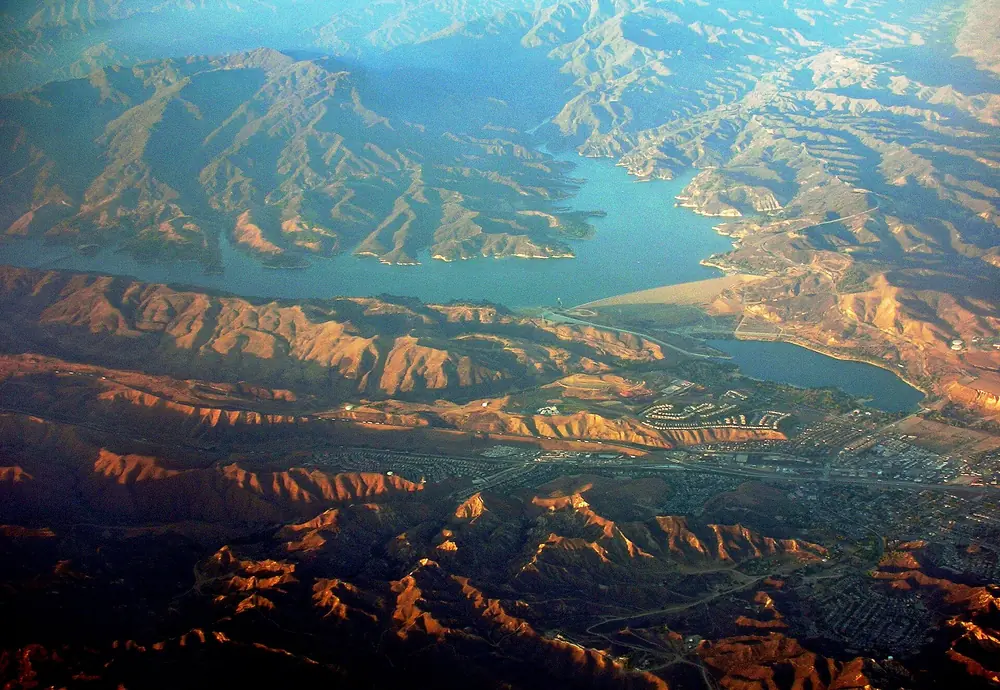 Aerial view of a reservoir among folded brown foothills in low evening light