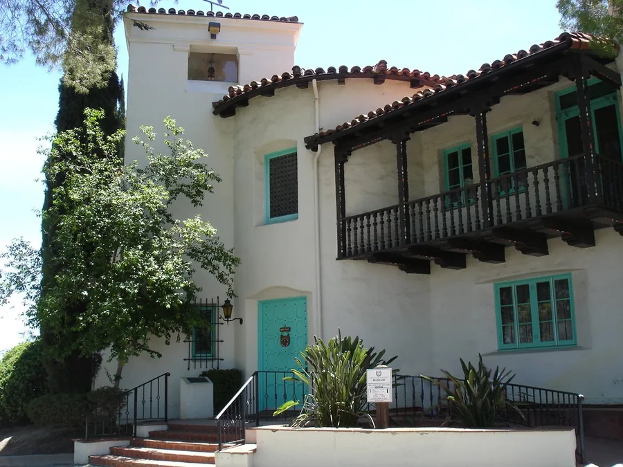 White Spanish Colonial Revival house with a wooden balcony and red tile roof at the Hart Ranch museum