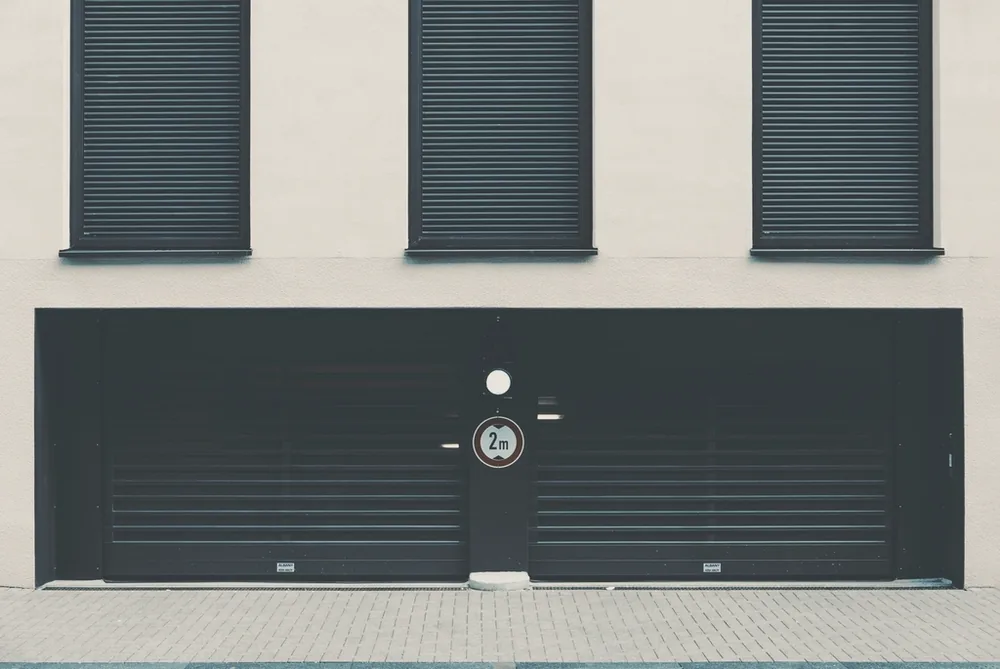 Wide flat black metal garage door with horizontal slats set into a pale wall