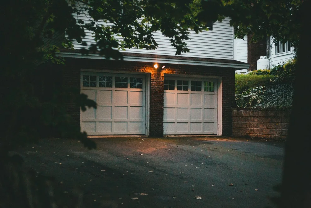 Two white carriage-style garage doors on a brick and siding house at dusk